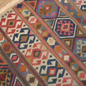Flatweave rug with diagonal bands of red, blue, and brown geometric patterns on light hardwood.