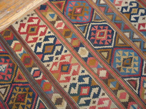 Flatweave rug with diagonal bands of red, blue, and brown geometric patterns on light hardwood.
