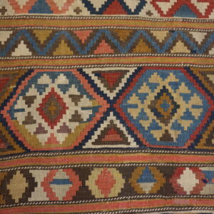 Geometric flatweave rug featuring horizontal bands of stepped diamonds and zig-zags in blue, red, and tan.