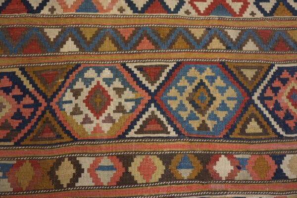 Geometric flatweave rug featuring horizontal bands of stepped diamonds and zig-zags in blue, red, and tan.