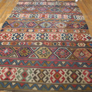 Multi-colored flatweave rug featuring geometric diamond and striped patterns on light hardwood planks.