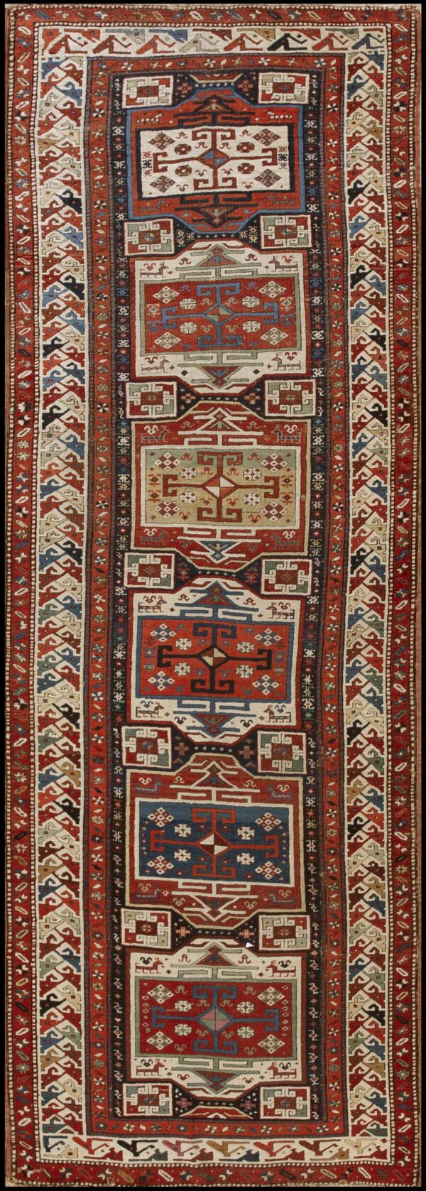 Long runner rug with repeating geometric medallions in red, navy blue, cream, and olive green, surrounded by complex tribal borders.