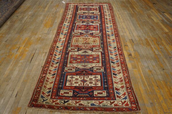 Geometric red and cream runner rug with blue accents sits on weathered light hardwood flooring.
