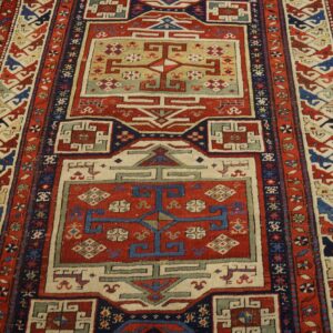 Red, blue, and cream geometric runner rug with tribal motifs lies on textured light brown wood flooring.