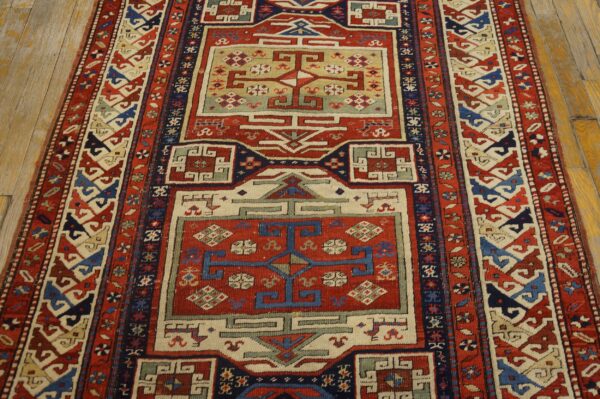 Red, blue, and cream geometric runner rug with tribal motifs lies on textured light brown wood flooring.
