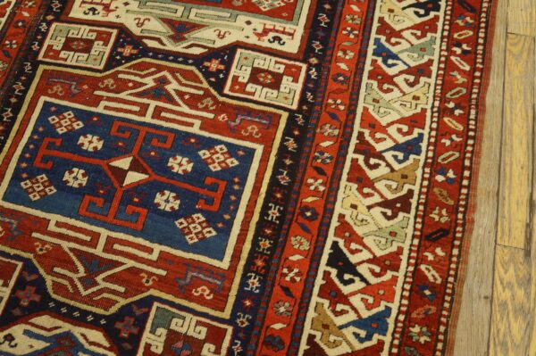 Low-pile rug with intricate red, blue, and cream geometric patterns rests on light wood flooring.
