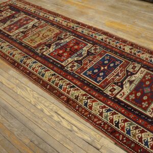 Red and blue geometric runner rug with repeating panels laid on rustic, light wooden floorboards.