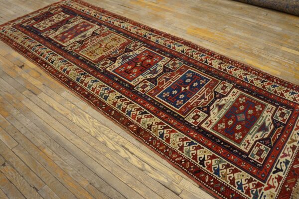 Red and blue geometric runner rug with repeating panels laid on rustic, light wooden floorboards.