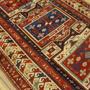 Low pile rug with bright red, navy, and cream geometric designs on light wood planks.