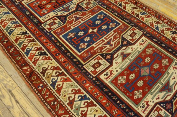 Low pile rug with bright red, navy, and cream geometric designs on light wood planks.