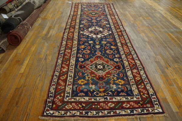 Low-pile blue runner rug featuring geometric medallions and multicolored borders on worn wooden floorboards.
