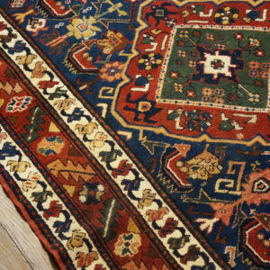 Geometric patterned rug in deep navy, red, green, and cream lies diagonally across weathered wooden floors.