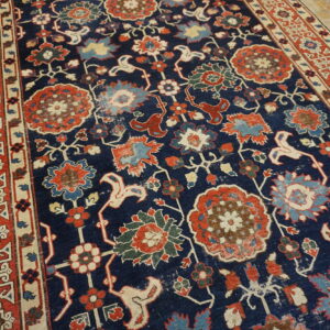 Traditional rug with a navy blue field and ornate red, blue, and cream floral patterns on light wood floors.