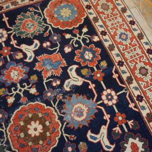 Close-up of a low pile navy rug featuring elaborate red and blue traditional floral designs on wood flooring.
