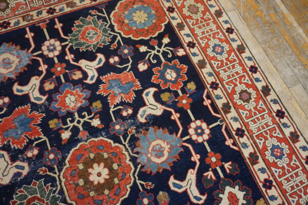 Close-up of a low pile navy rug featuring elaborate red and blue traditional floral designs on wood flooring.