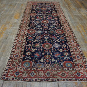 Ornate navy blue runner rug with complex red and multi-colored floral designs on distressed wood flooring.