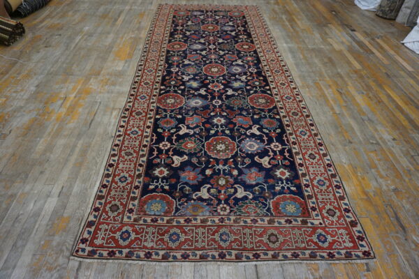 Ornate navy blue runner rug with complex red and multi-colored floral designs on distressed wood flooring.