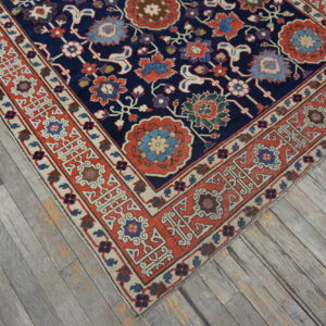 Navy blue floral rug with red, blue, and cream accents rests on gray weathered plank flooring.