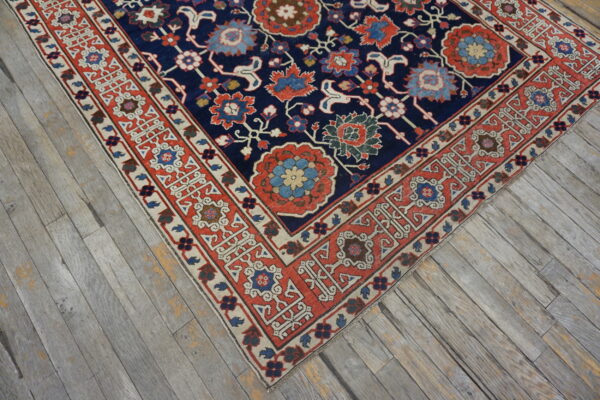Navy blue floral rug with red, blue, and cream accents rests on gray weathered plank flooring.