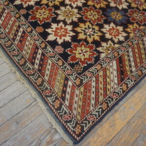 Rug corner with navy field, repeating red and cream floral medallions, and multicolored borders on gray wood.