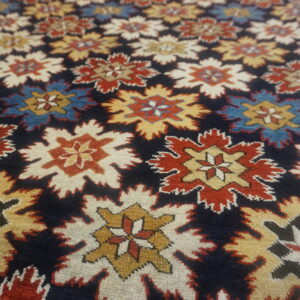 Close-up of a high-pile rug featuring repeating red, gold, blue, and cream serrated medallions on a dark navy field.