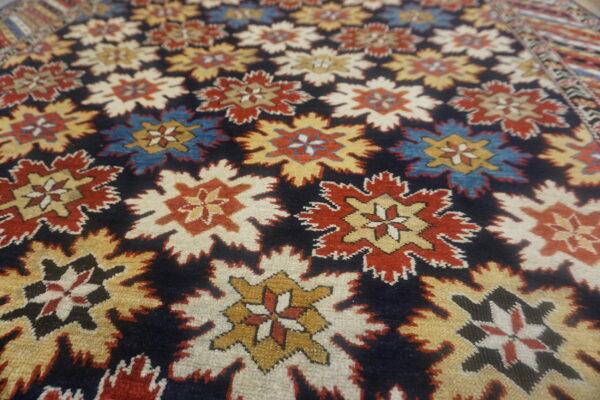 Close-up of a high-pile rug featuring repeating red, gold, blue, and cream serrated medallions on a dark navy field.