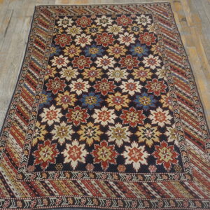 Traditional rug with repeating red, beige, and blue star patterns on a dark ground, lying on weathered wood floors.
