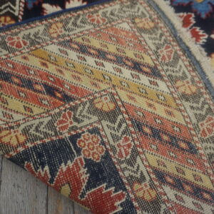 Close-up showing the flat woven backing and navy, red, white pile of a rug on wood.