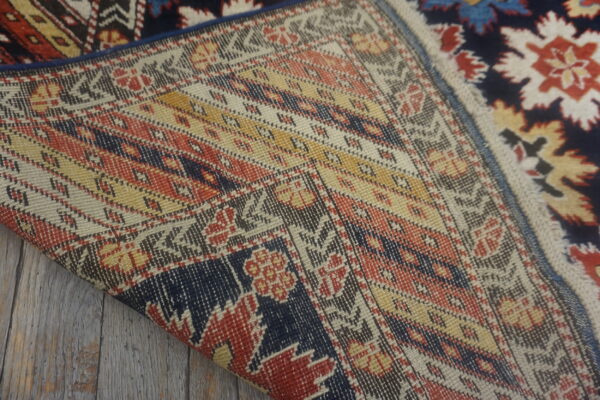 Close-up showing the flat woven backing and navy, red, white pile of a rug on wood.