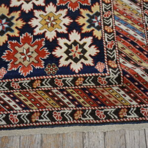 Geometric navy, red, and cream star patterns decorate a rug lying on rustic gray wood planks.
