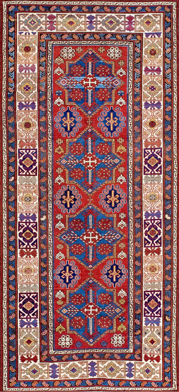 Red rug with large blue geometric medallions and wide, colorful, contrasting patterned borders.