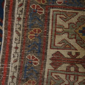 Close view of geometric rug patterns featuring muted tan, dark red, blue, and brown low-pile weaving.
