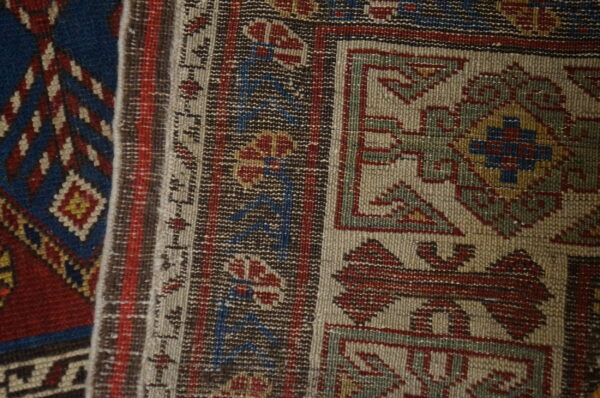 Close view of geometric rug patterns featuring muted tan, dark red, blue, and brown low-pile weaving.