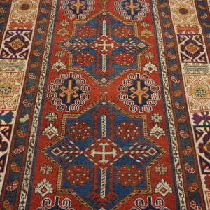 Geometric runner rug with blue and cream medallions on a red field over pale wood planks.