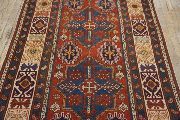 Geometric runner rug with blue and cream medallions on a red field over pale wood planks.
