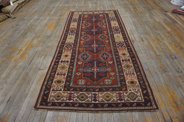 Geometric runner rug in red, navy, and cream with multiple ornate borders on distressed wood planks.