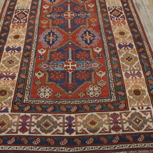 Geometric red and blue area rug with a complex wide border displayed on distressed light wood planks.