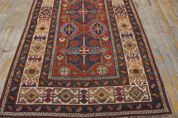 Geometric red and blue area rug with a complex wide border displayed on distressed light wood planks.