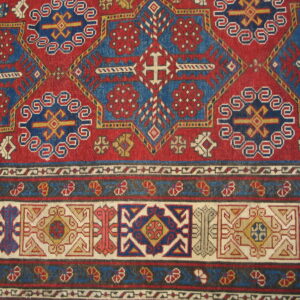 Detailed geometric rug pattern features alternating red and blue sections with multicolored, stacked border designs.