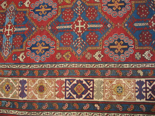 Detailed geometric rug pattern features alternating red and blue sections with multicolored, stacked border designs.