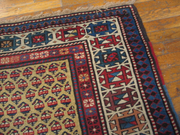 Geometric rug corner showing a yellow field with boteh motifs and red and blue borders on plank wood.