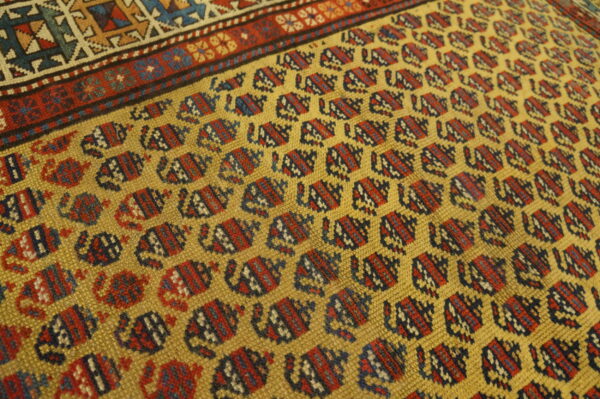 Textured golden yellow rug featuring repeating red and blue geometric patterns near a multicolored border.