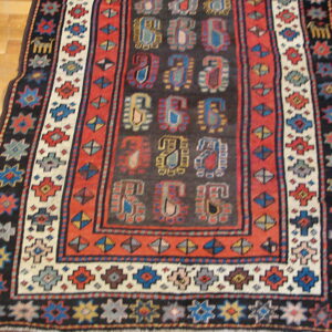 Stylized multicolored paisley patterns fill the dark field of this geometrically bordered rug on wood floor.