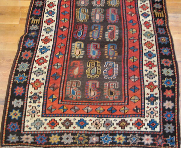 Stylized multicolored paisley patterns fill the dark field of this geometrically bordered rug on wood floor.