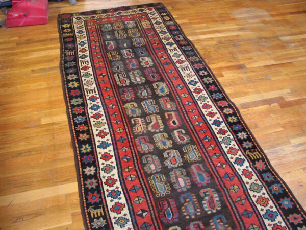 Dark runner rug featuring vibrant red, blue, and cream geometric patterns rests on a honey-toned wood floor.