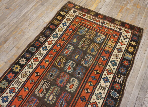 Dark brown and rust tribal rug featuring blue and cream medallions and borders on light plank flooring.