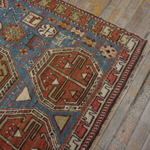 Blue and rust geometric rug with intricate patterns lies on aged, wide-plank hardwood flooring.