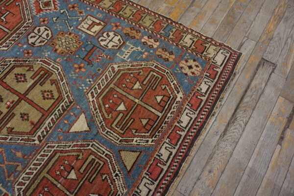 Blue and rust geometric rug with intricate patterns lies on aged, wide-plank hardwood flooring.