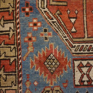Detail of a low-pile rug featuring blue, red, tan, and black geometric patterns on rustic wood.