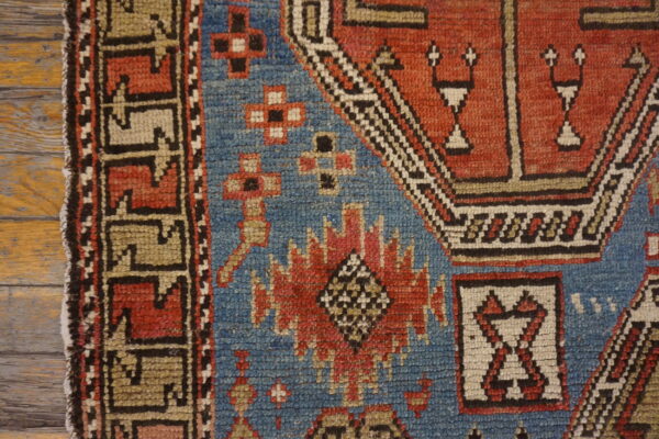 Detail of a low-pile rug featuring blue, red, tan, and black geometric patterns on rustic wood.